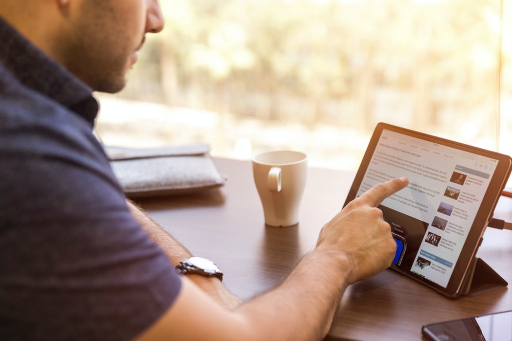 man-sitting-at-table-with-coffee-cup-while-scrolling-through-LinkedIn-on-upright-tablet